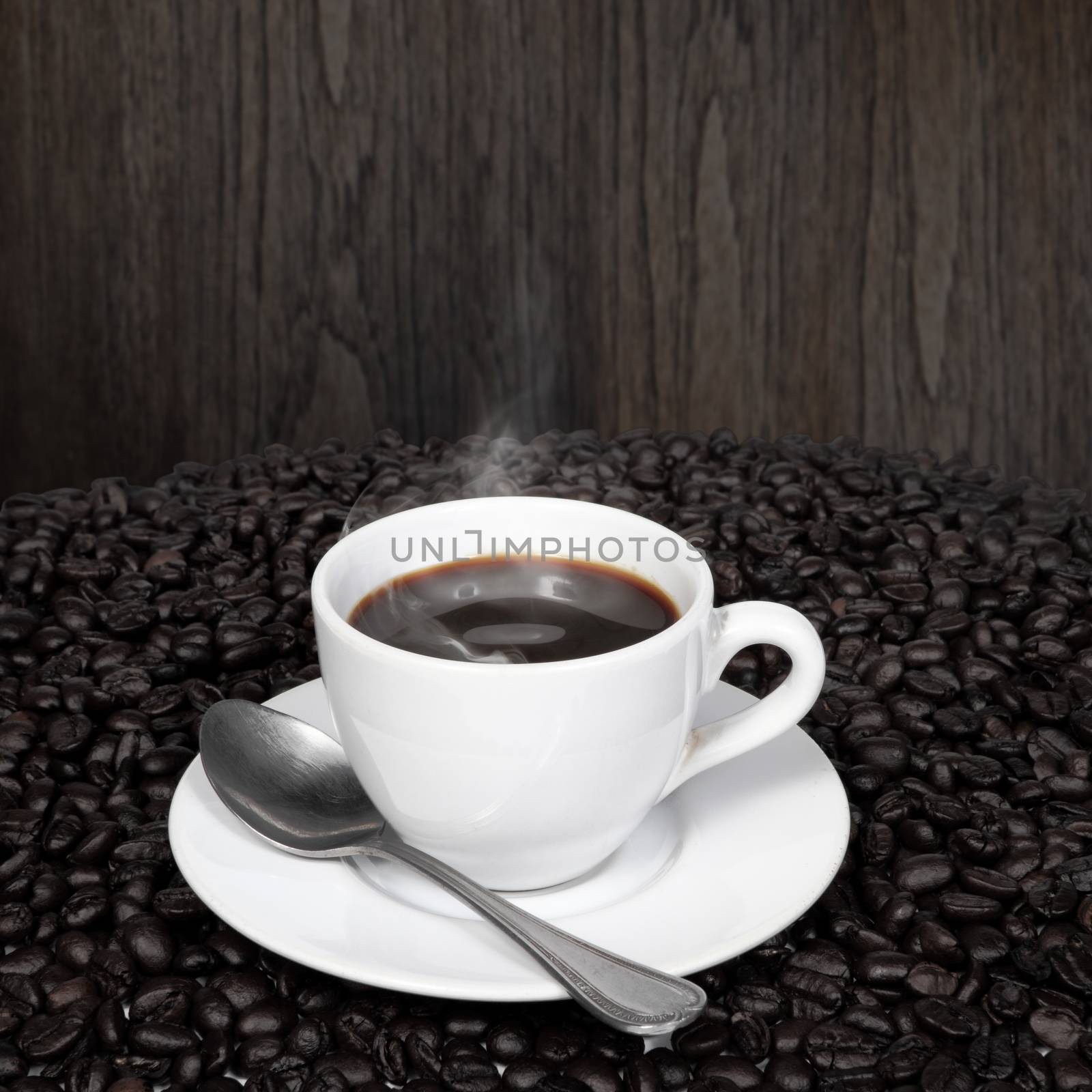 Black coffee in cup and coffee beans with smoke on old wood background.