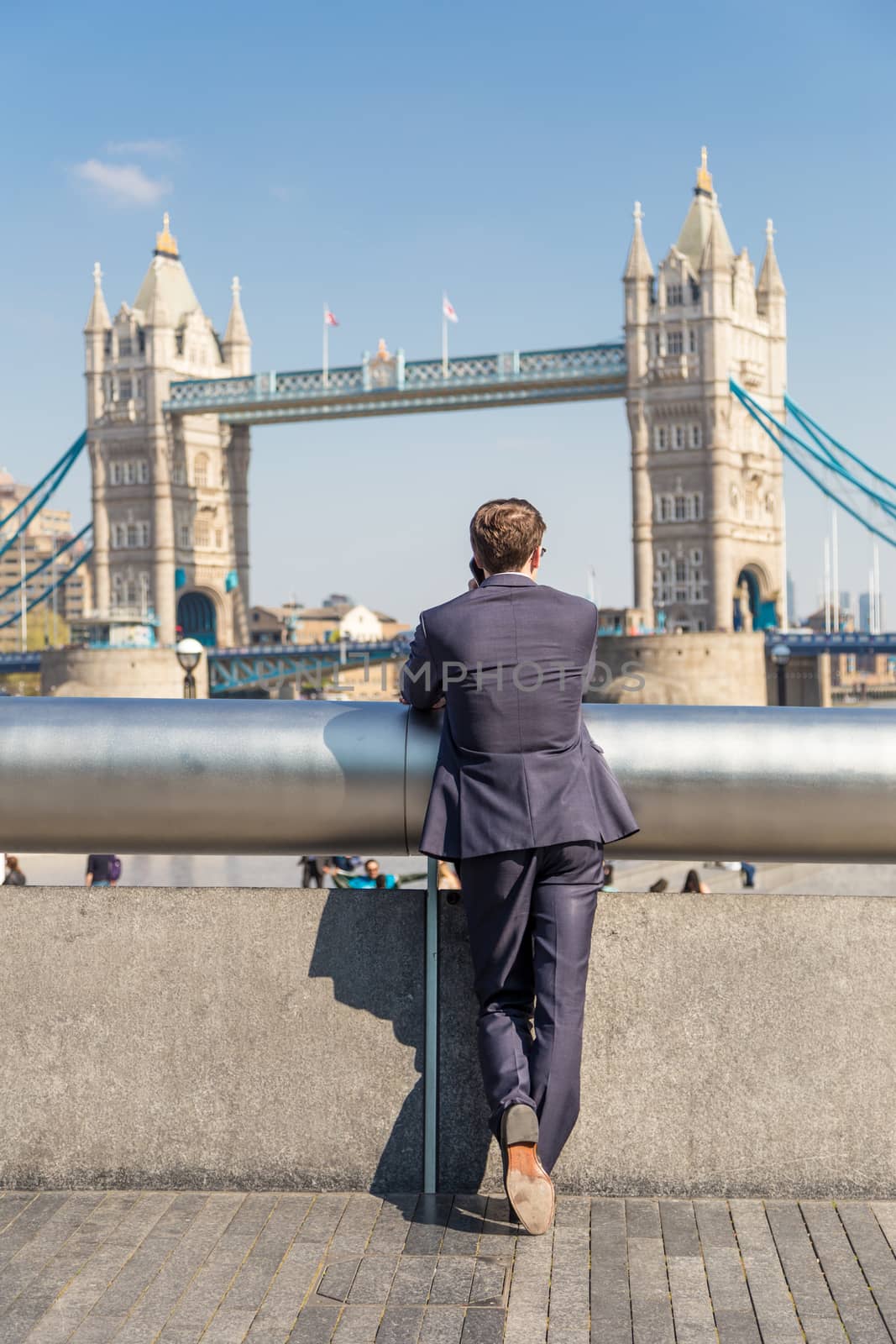 Businessman talking on mobile phone outdoor, looking at Tower Bridge in London city, UK.