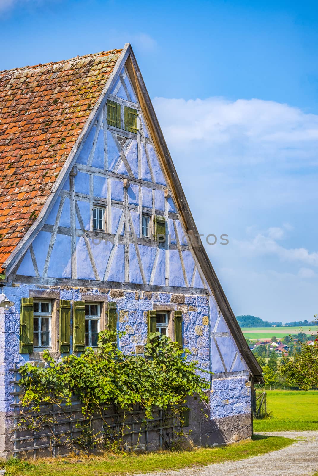 Antique house with German specific architecture, half timbered and stone walls of blue color, windows with wooden shutters and tile gable roof.