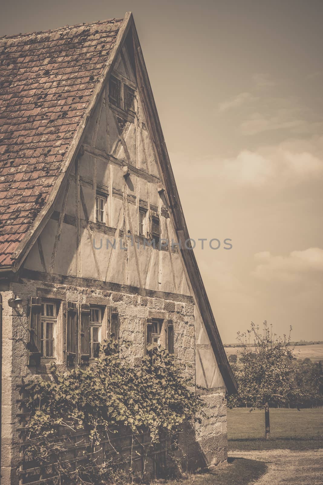 Retro style image of an antique german house with traditional architecture, gable roof, half timbered wall for the loft and stone wall, wooden shutters and vine bushes for the ground floor.