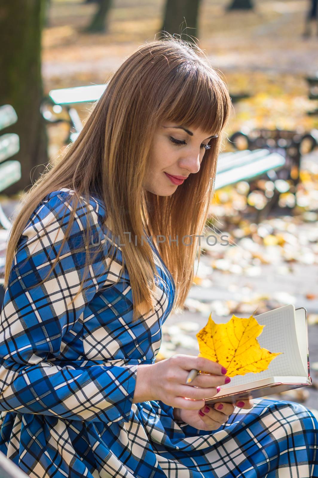 beautiful girl with long straight hair in a blue long dress reading a book in the autumn park