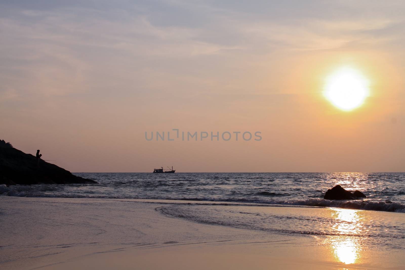 a silhouette of a fisher at sunset on a seashore. Sunset landscape of sea with fisherman standing on rock, southern Thailand, Phuket Island