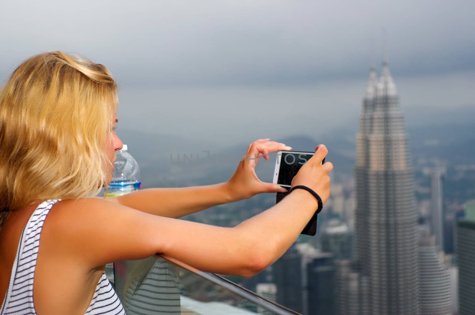 KUALA LUMPUR, MALAYSIA - January 17, 2016: Travel and technology. Young woman taking photo with smartphone from KL- Tower at evening. by evolutionnow