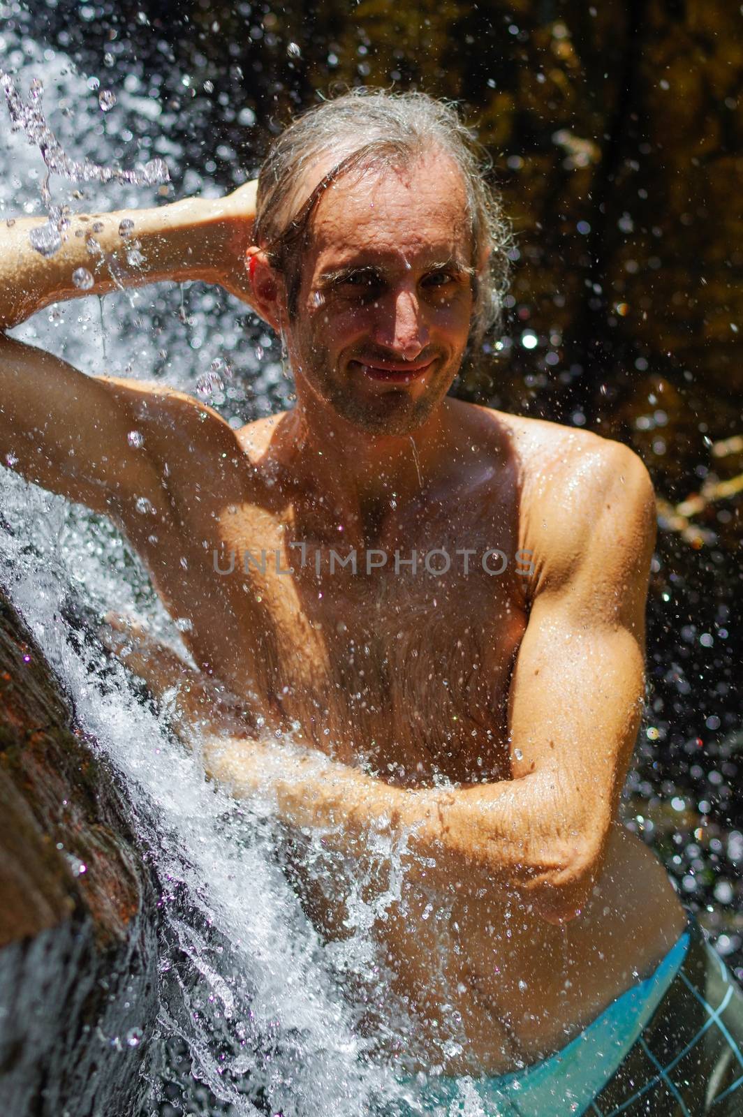 Man taking a relaxing shower under waterfall. outside by evolutionnow