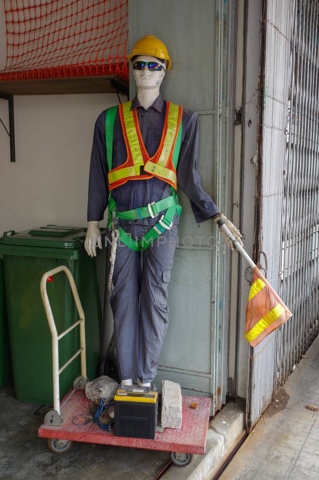 a Mannequins of a worker outside with a wheelbarrow and car battery in front,Display dummy.