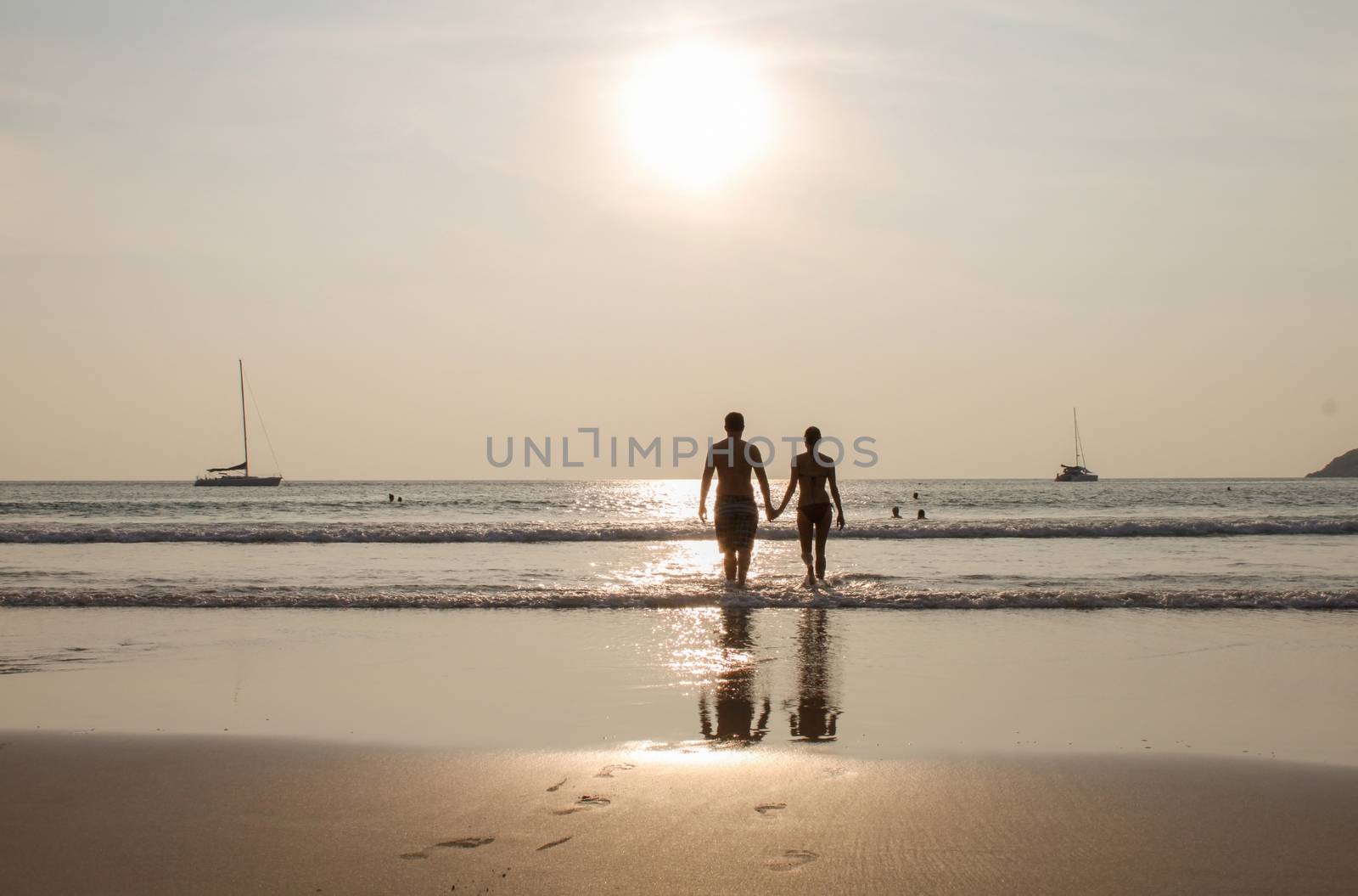 Silhouette of couple walking on beach at sunset holding hands. Horizontally framed shot. by evolutionnow