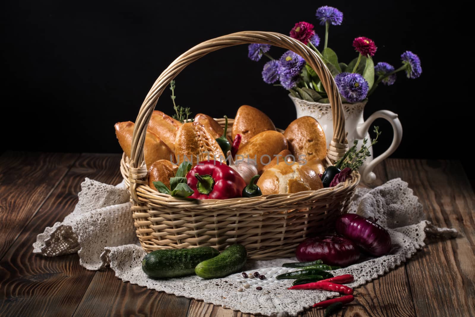 Wicker basket with vegetables and pastries, tablecloth and vase with flowers on an old wooden desk
