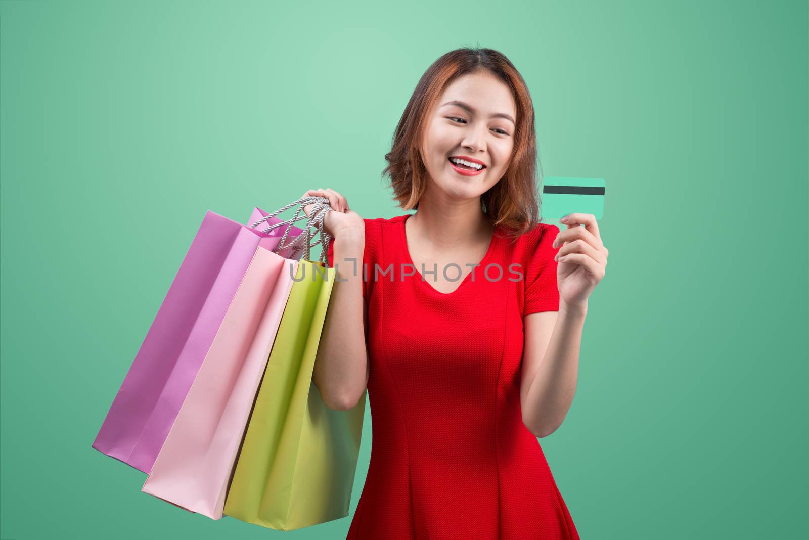 Santa asian woman holding shopping bags and credit card against blue vignette