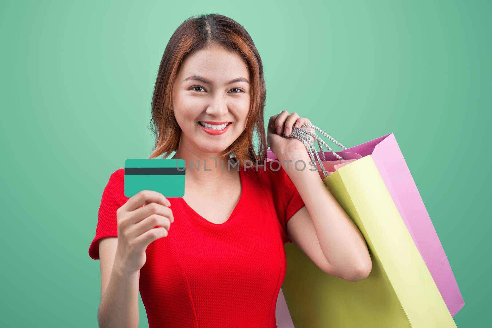 Santa asian woman holding shopping bags and credit card against blue vignette
