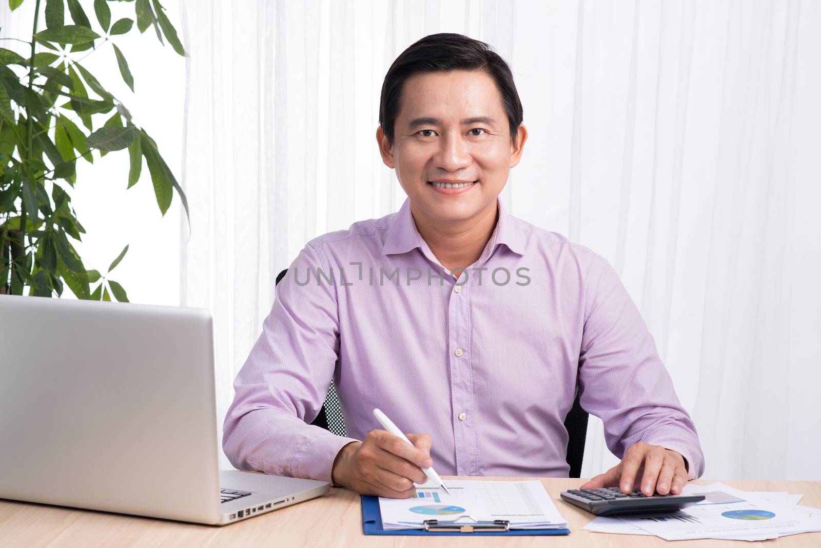 Smiling businessman at his desk with laptop and documents in his office