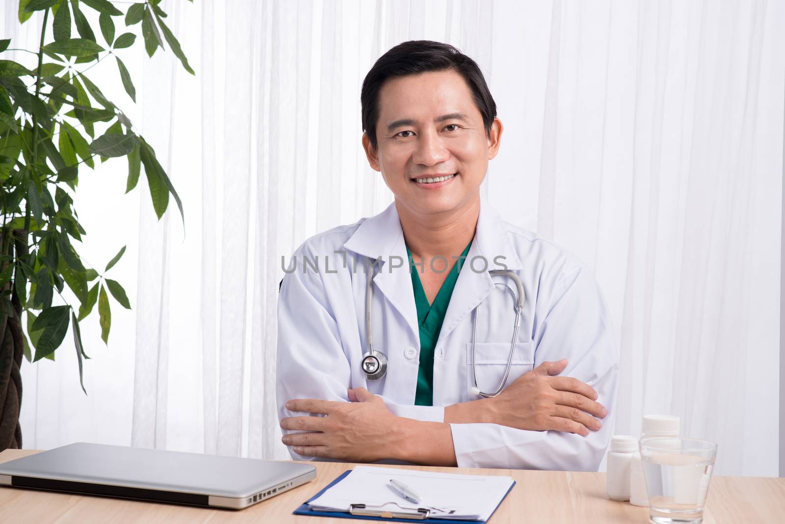 Smiling doctor sitting at his desk in medical office writing prescription 