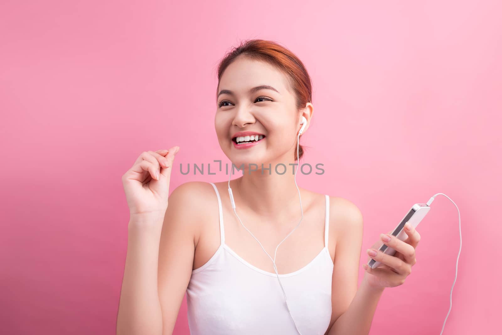 Happy asian girl dancing and listening to the music isolated on a pink background