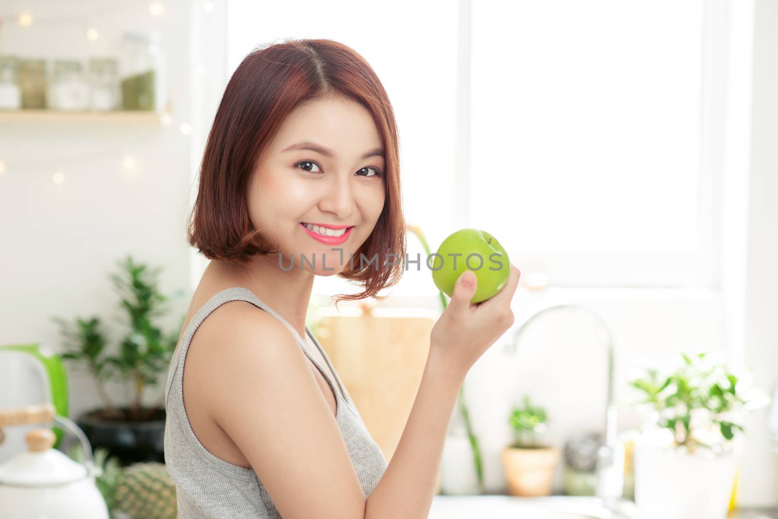 Happy Young Asian Woman Eating Green Apple on Kitchen. Diet. Die by makidotvn