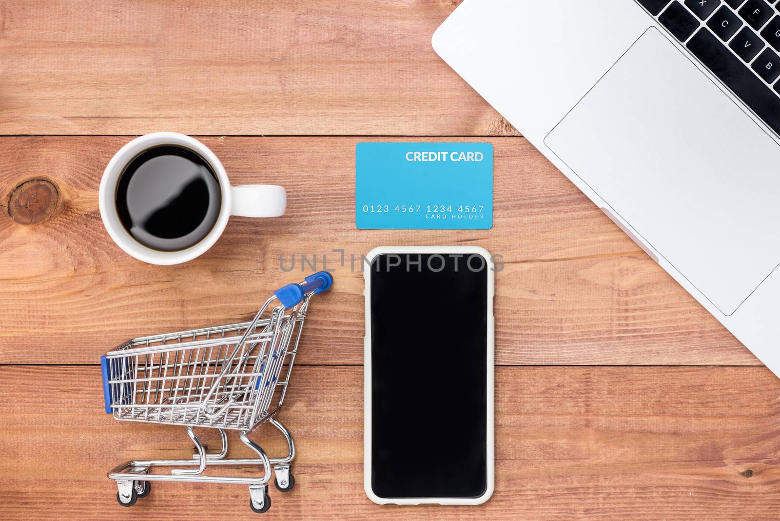 Shopping online concept. Small blue trolley and gadgets on the wooden table.