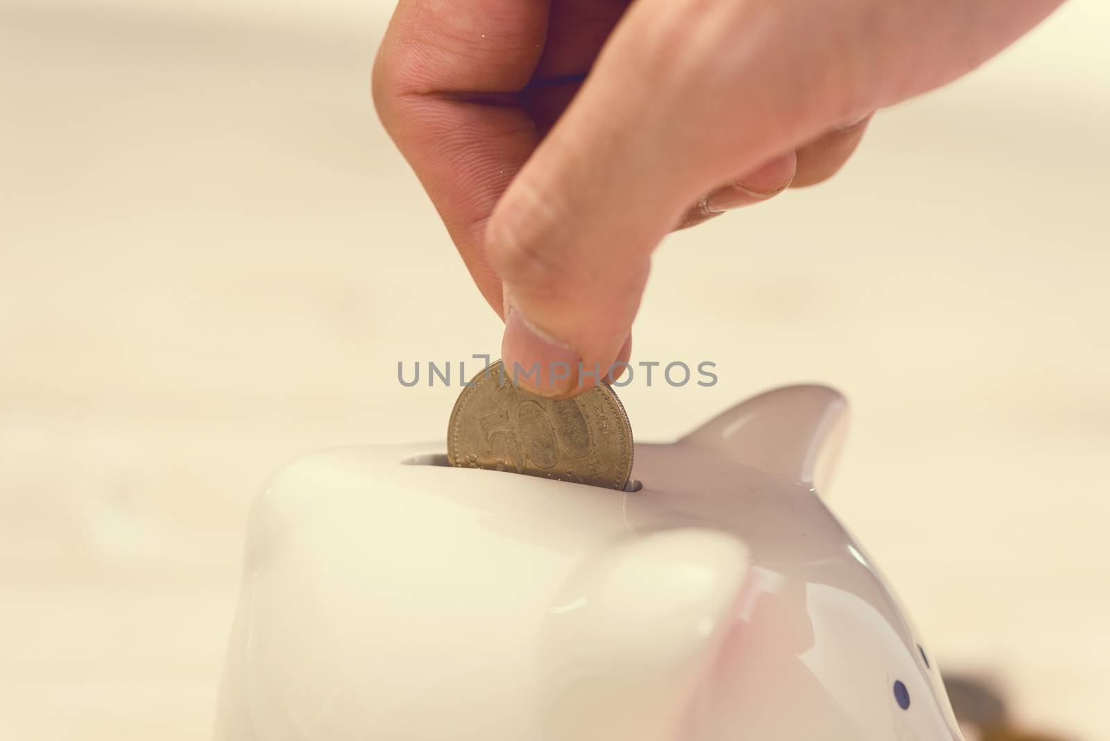 Hand putting golden coins into a pink piggy bank. Japanese Yen.