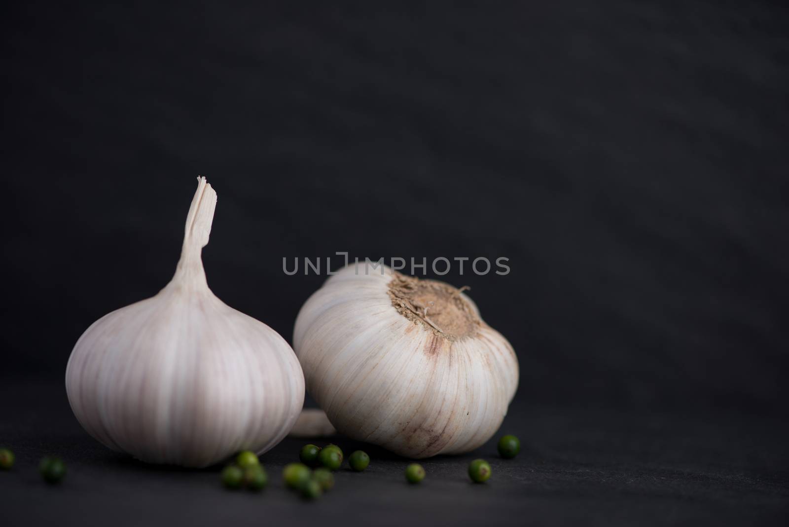 Garlic and green peppercorns on the black stone table by makidotvn