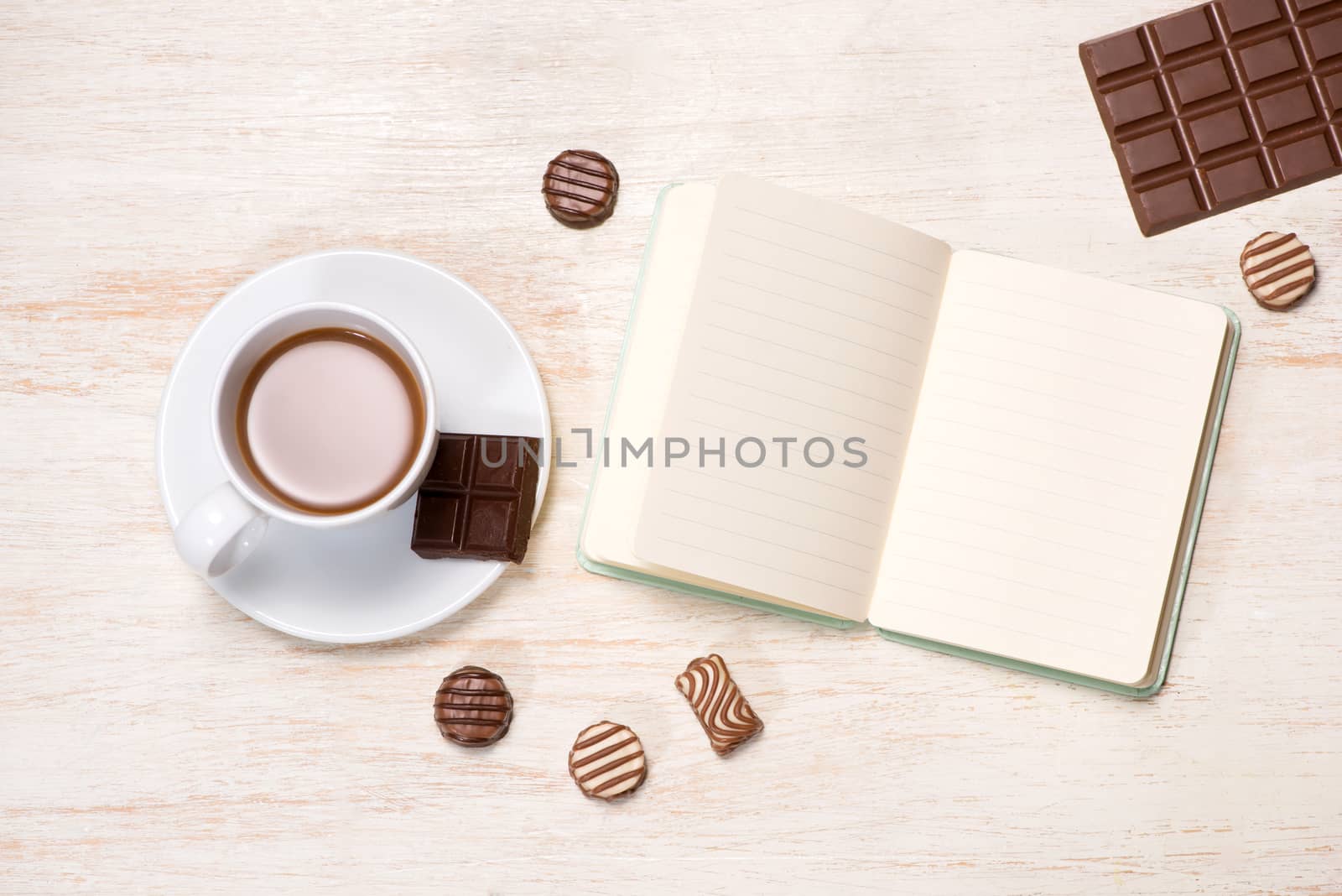 Coffee milk cup and delicious chocolates with notebook on table.