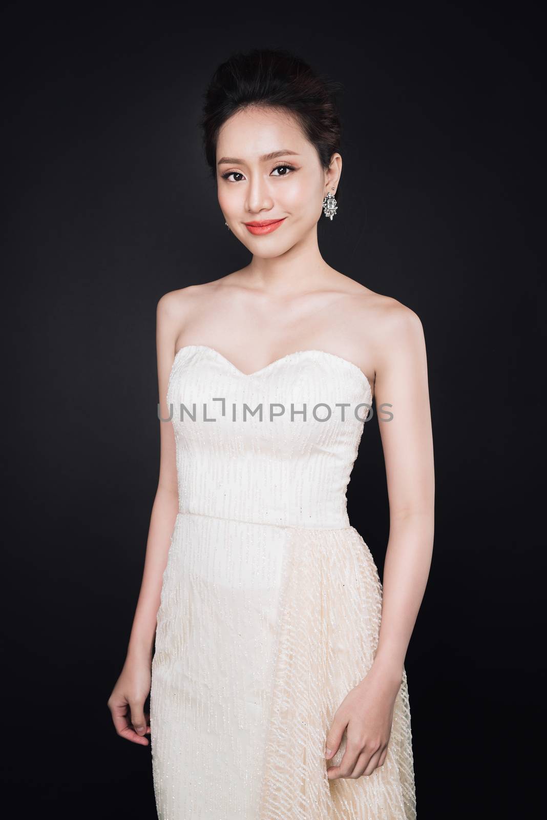 Fashion portrait of beautiful young asian woman in white dress over dark background.