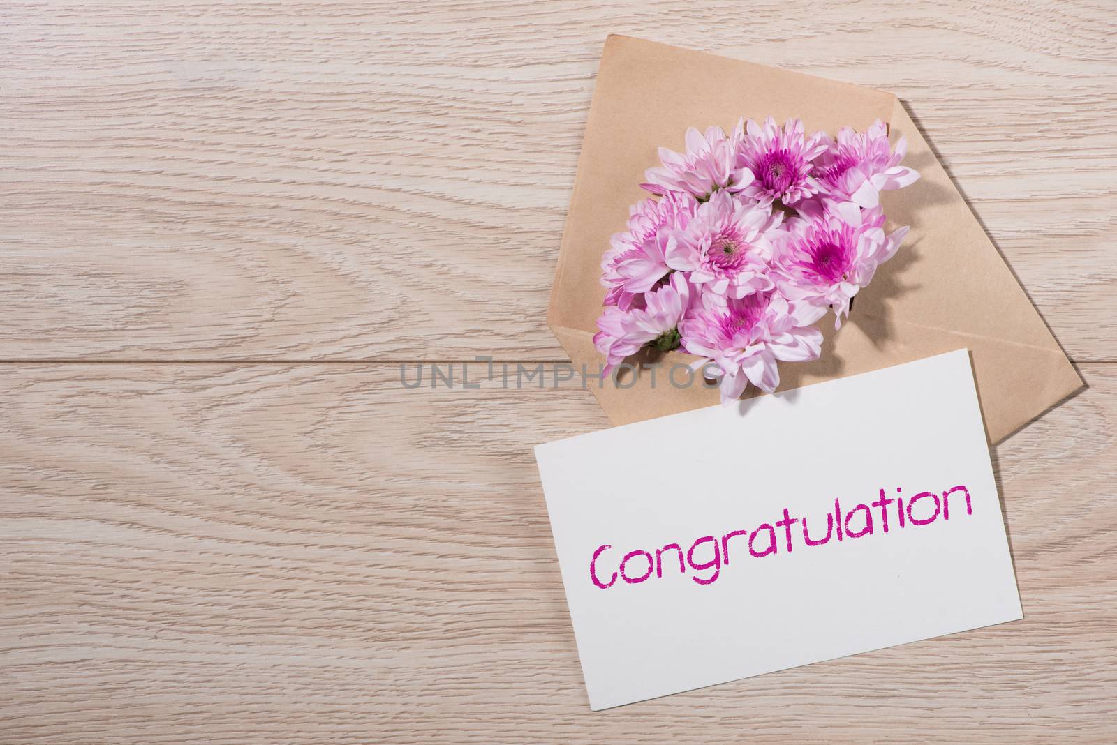 Blank white paper tag with brown envelope and pink flowers on wooden table.