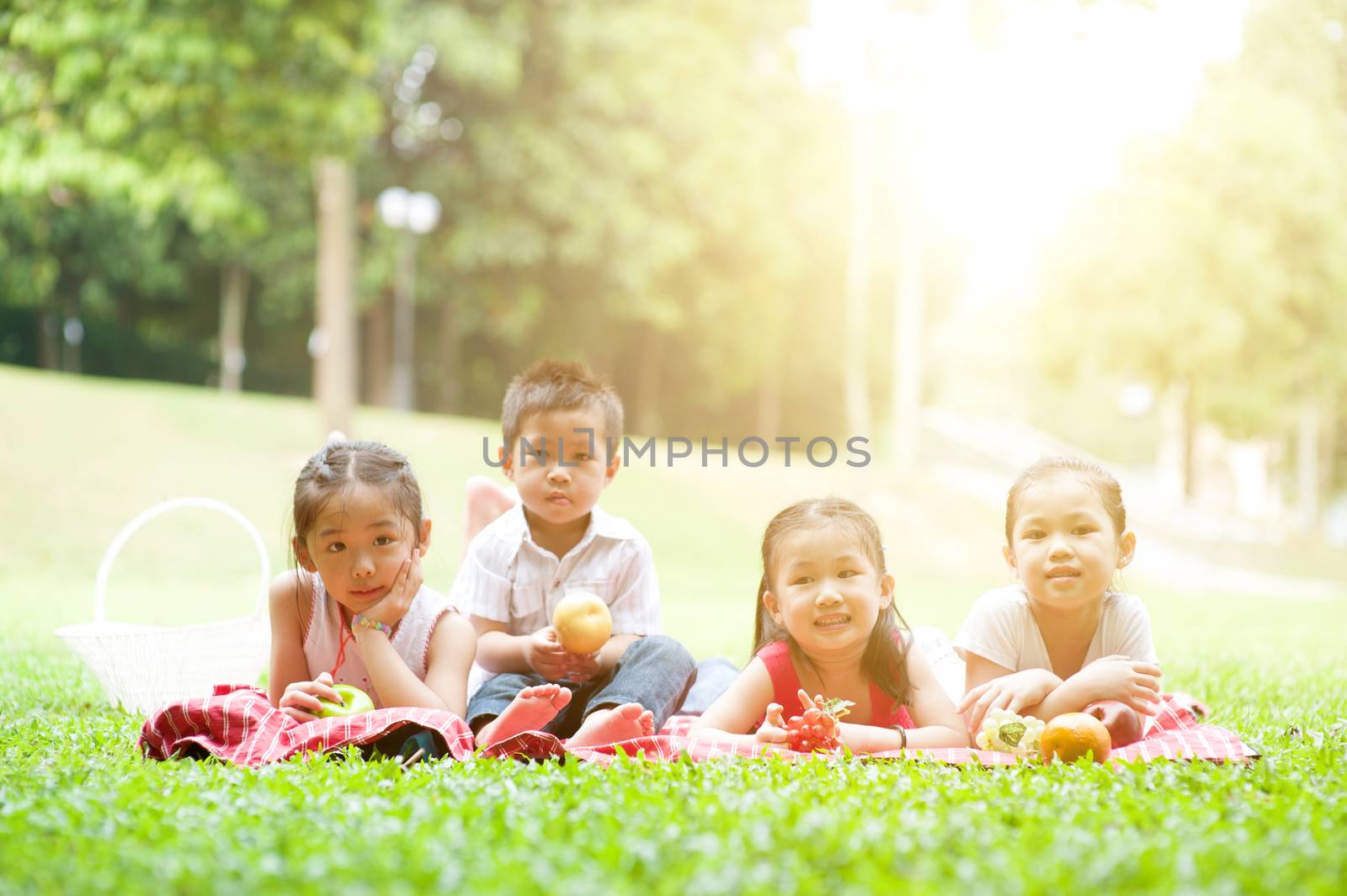 Portrait of Asian children picnics at park, lying on lawn. Kids having fun outdoors. Morning sun flare background.