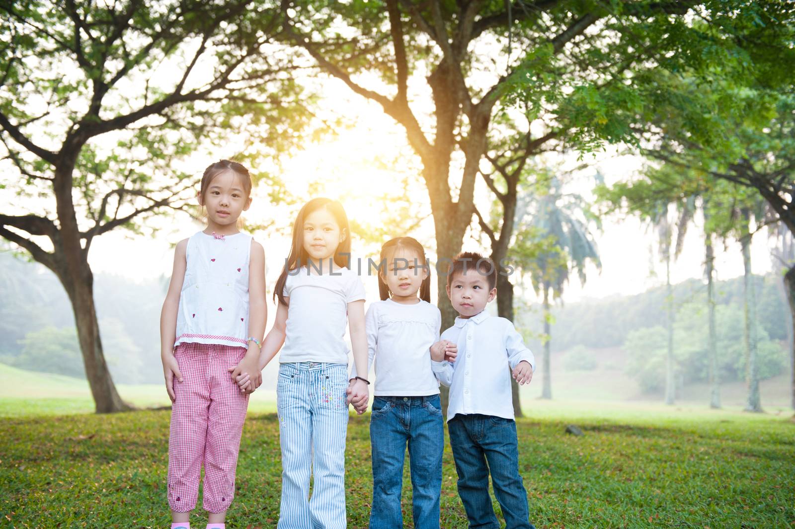 Portrait of Asian children holding hands at park. Little girls and boy having fun outdoors. Morning sun flare background.