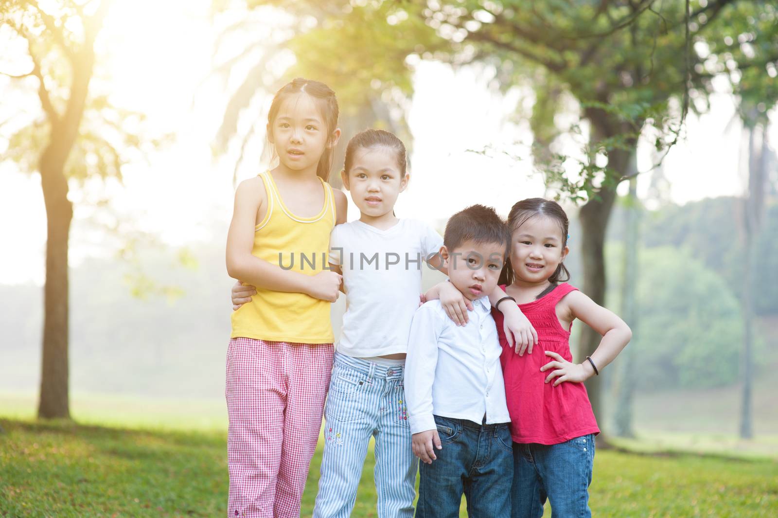 Portrait of four Asian children at park. Little girls and boy having fun outdoors. Morning sun flare background.