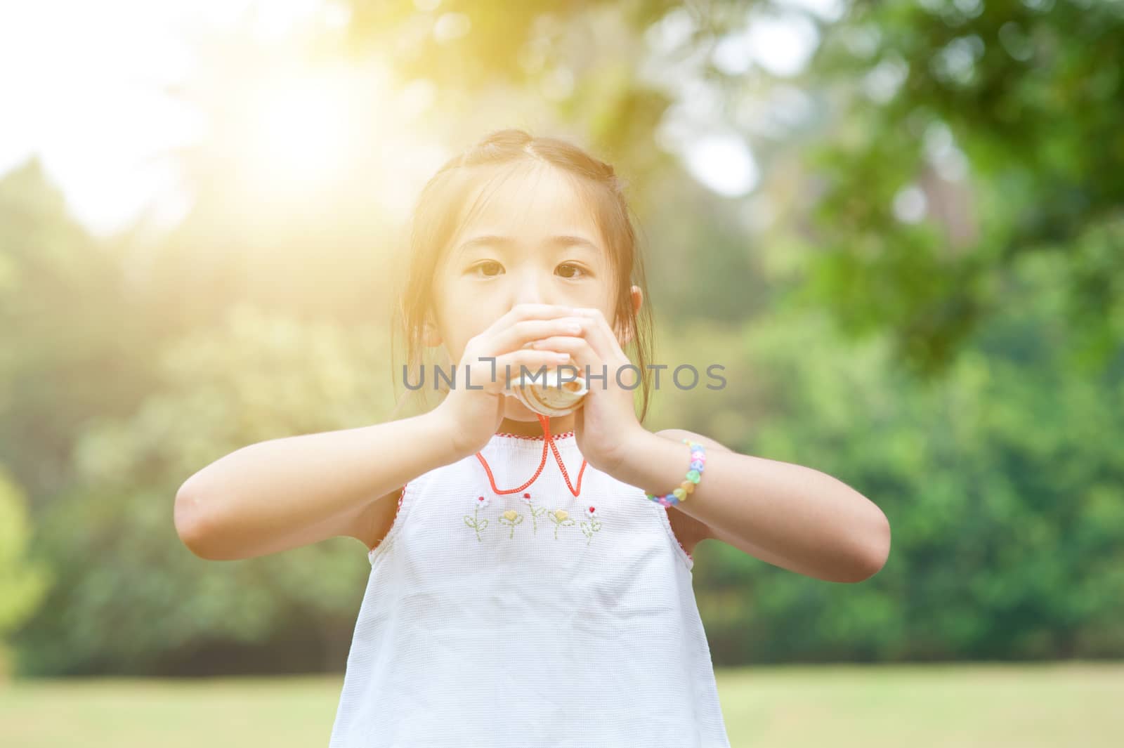 Portrait of Asian kid playing toy at park. Little girl having fun outdoors. Morning sun flare background.
