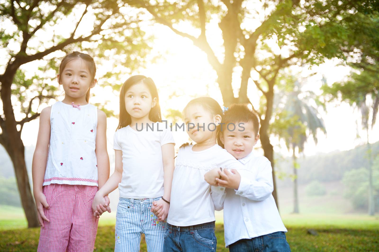 Portrait of Asian children at park. Little girls and boy having fun outdoors. Morning sun flare background.