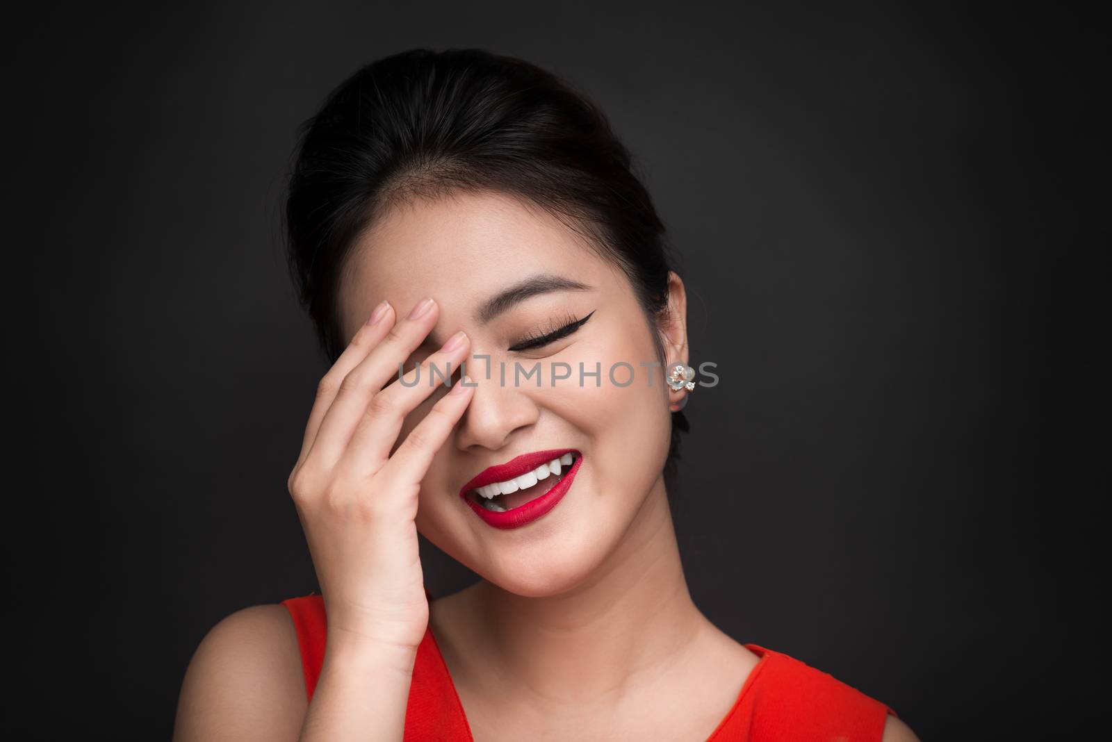Smiling shy woman closed her face with a hand over black background.