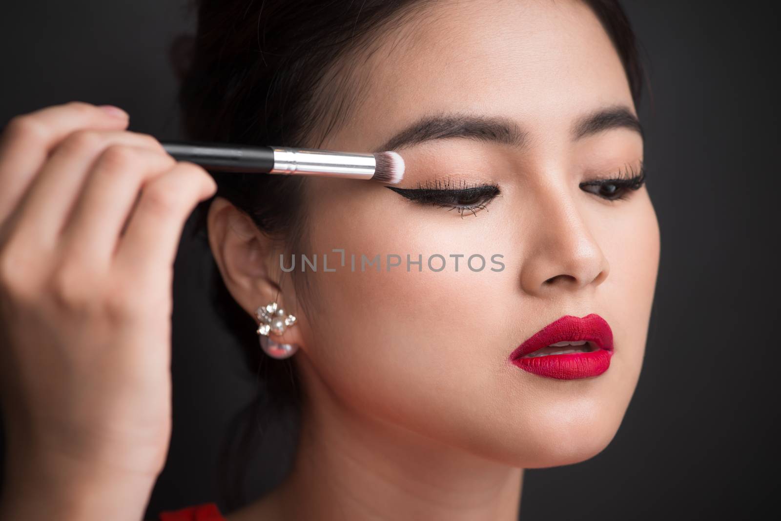 Close up of hand of asian woman applying eyeshadow on female eyelid.