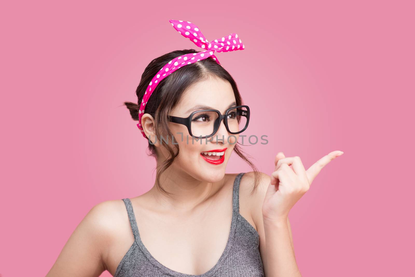 Young asian with pin-up make-up pointing to space over pink background.