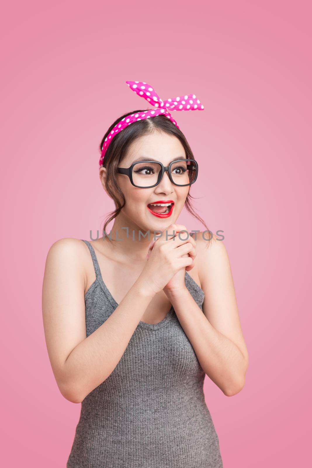 Portrait of beautiful asian woman eating heart shape lollipop, dressed and makeup in pin-up style on pink background.