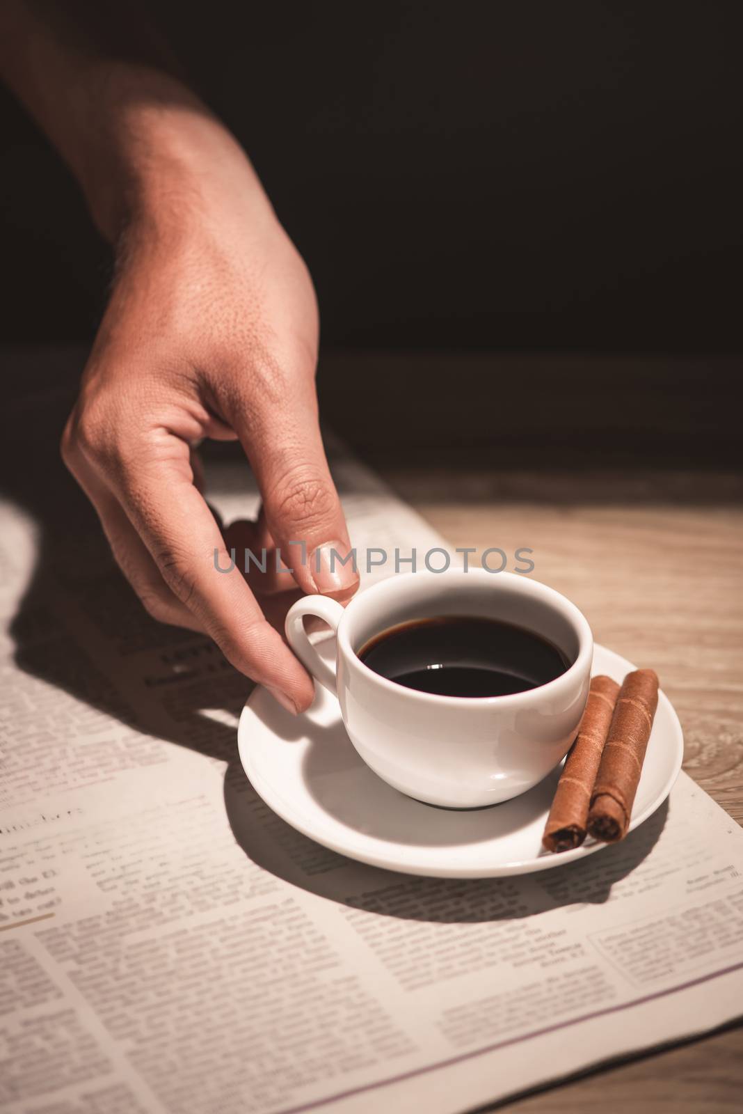 Male hands holding a cup of coffee over wooden table.