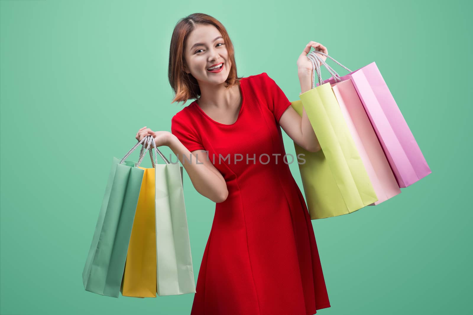 Beautiful young asian woman with colored shopping bags over blue background