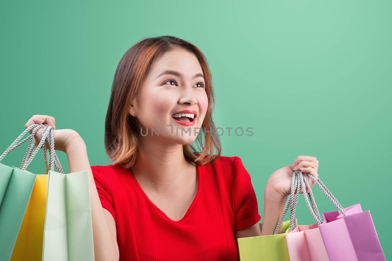 Beautiful young asian woman with colored shopping bags over blue background