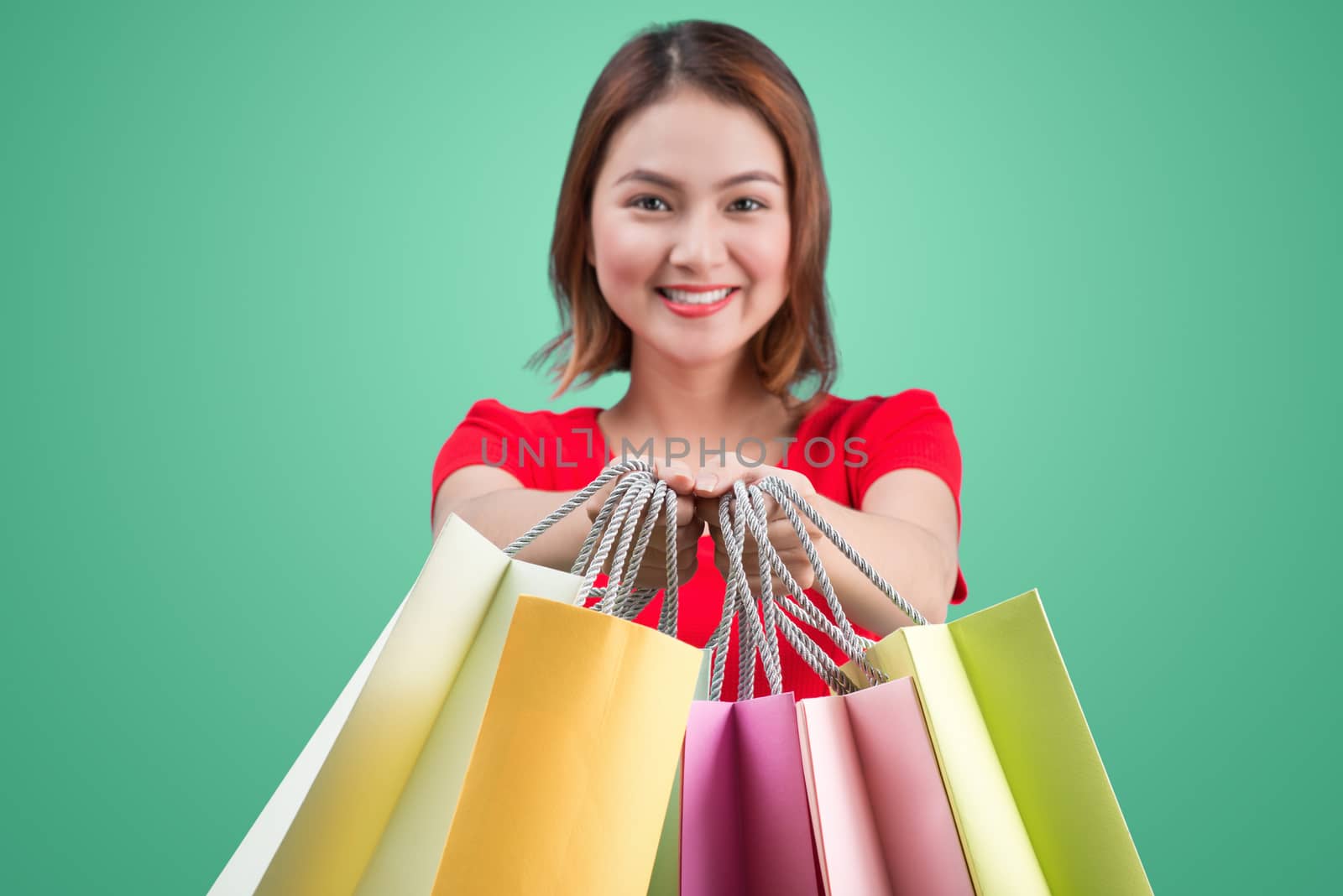 Beautiful young asian woman with colored shopping bags over blue background. Focus on bags.