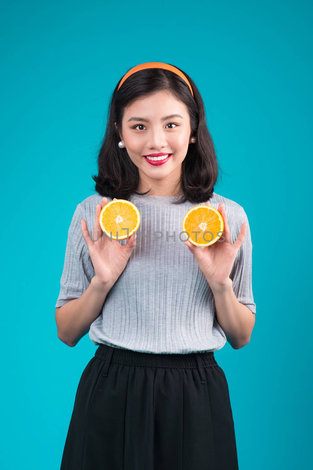 Healthy food. Smiling lovely pinup asian girl holding orange over blue background.