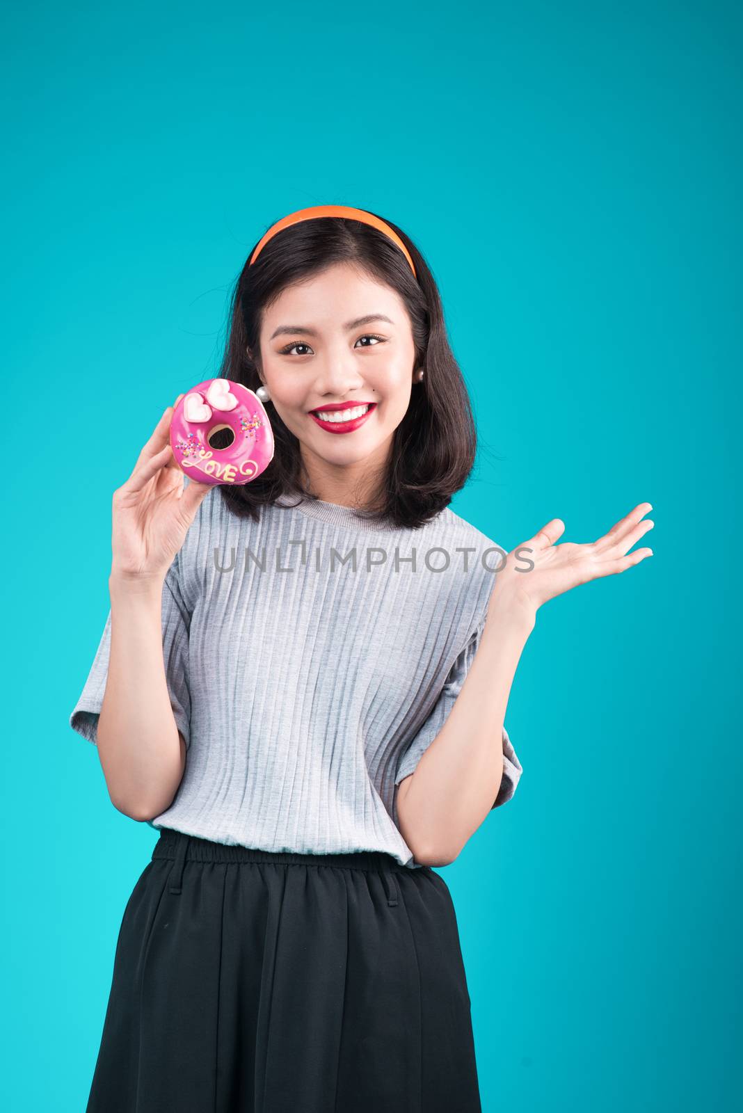 Asian beauty girl holding pink donut. Retro joyful woman with sweets, dessert standing over blue background.