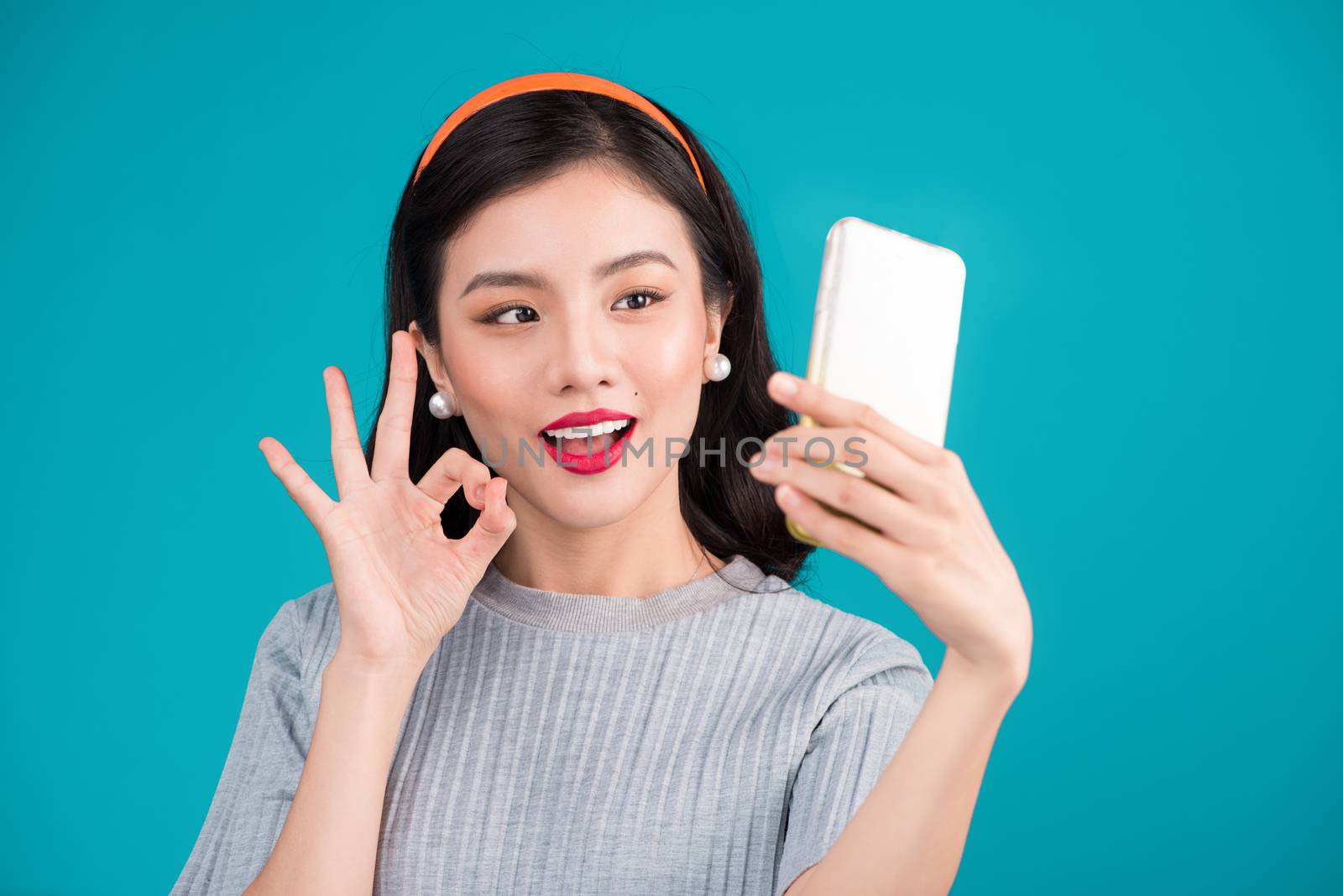 Close-up of smiling lovely pinup asian girl taking selfie photo over blue background.