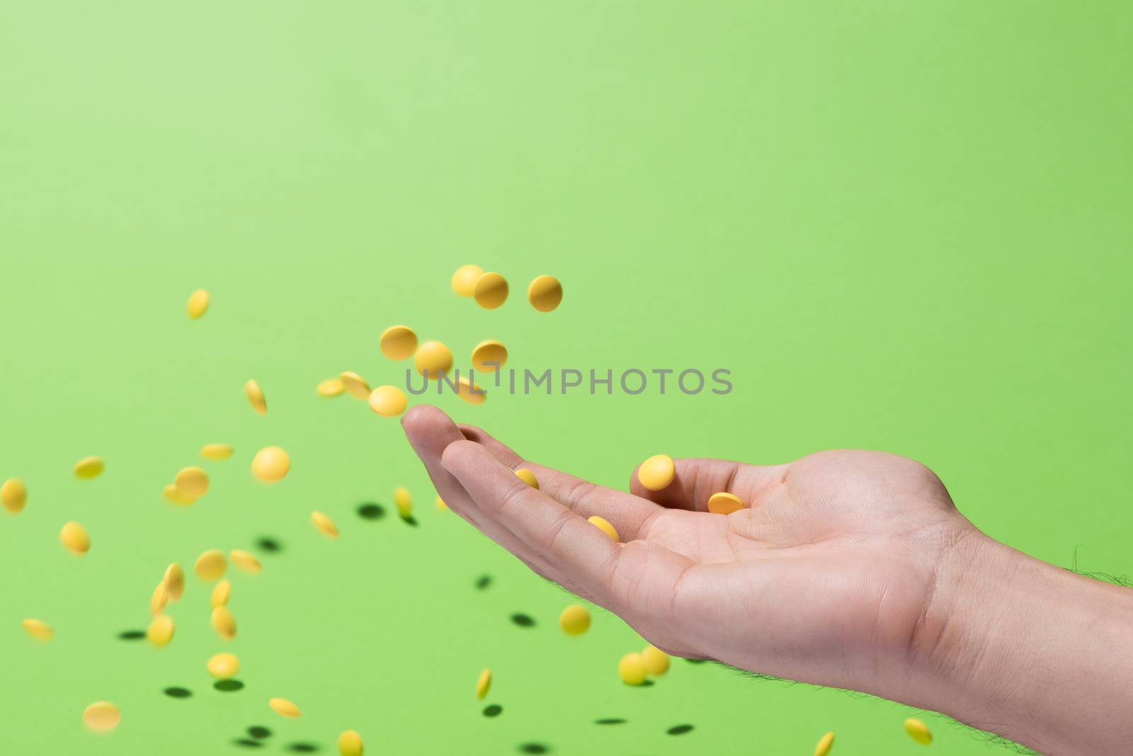 Flying yellow pills from hand in front of green background