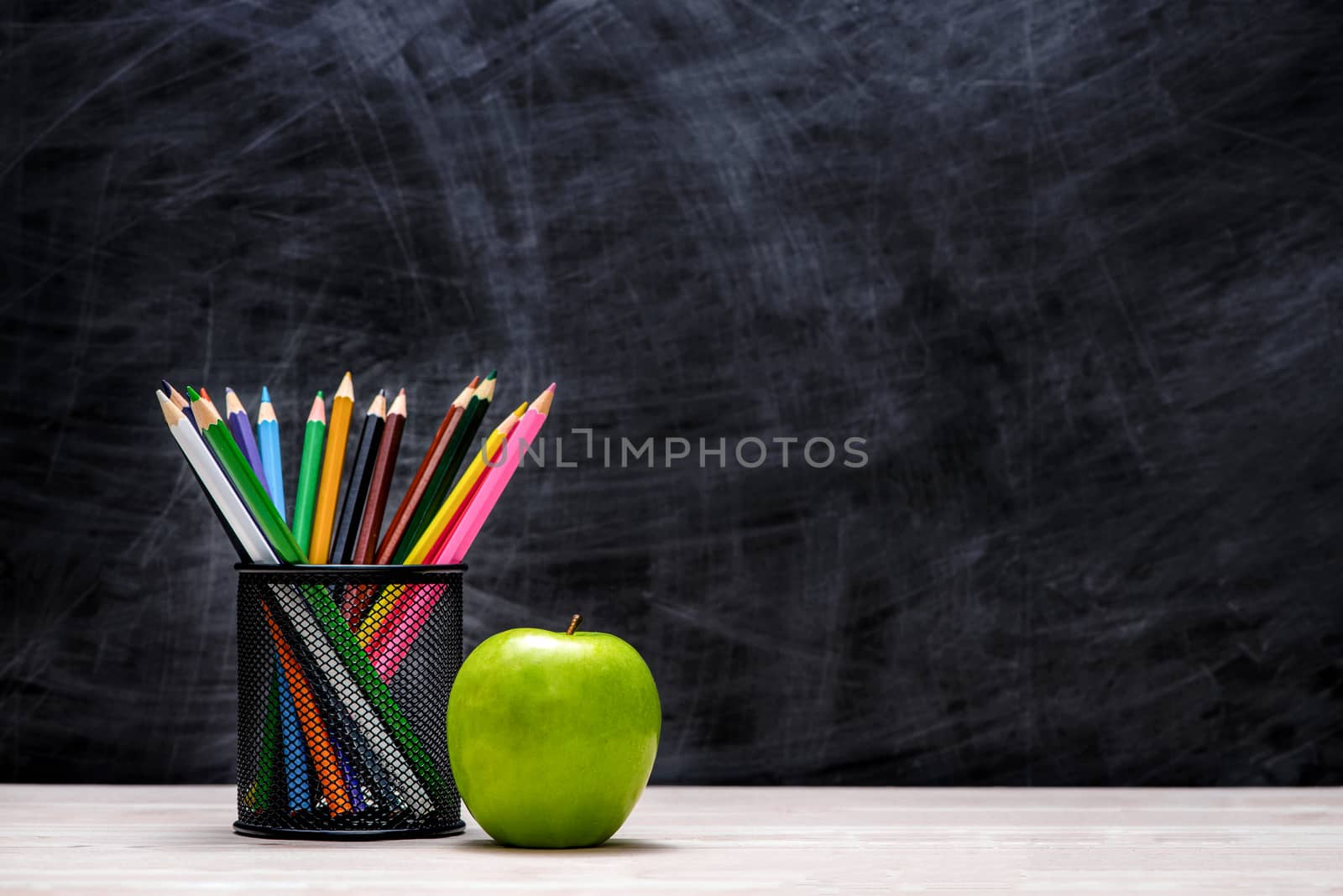 School and office supplies and apple in front of blackboard.