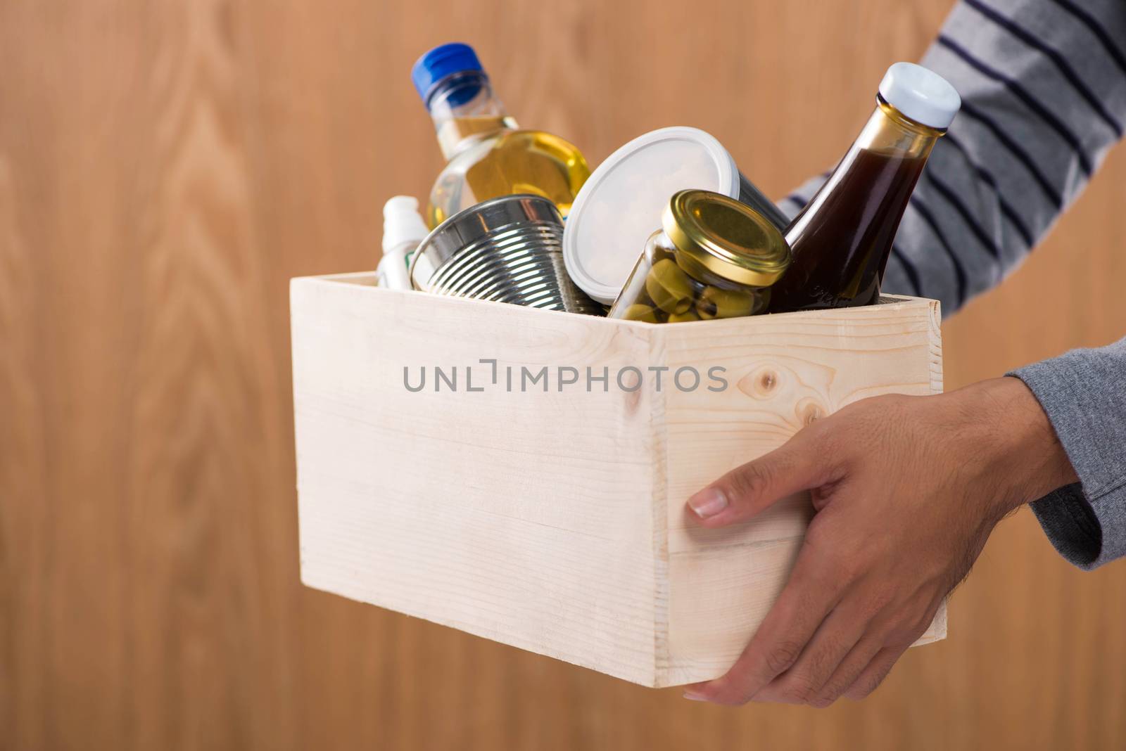 Volunteer with donation box with foodstuffs on wooden background