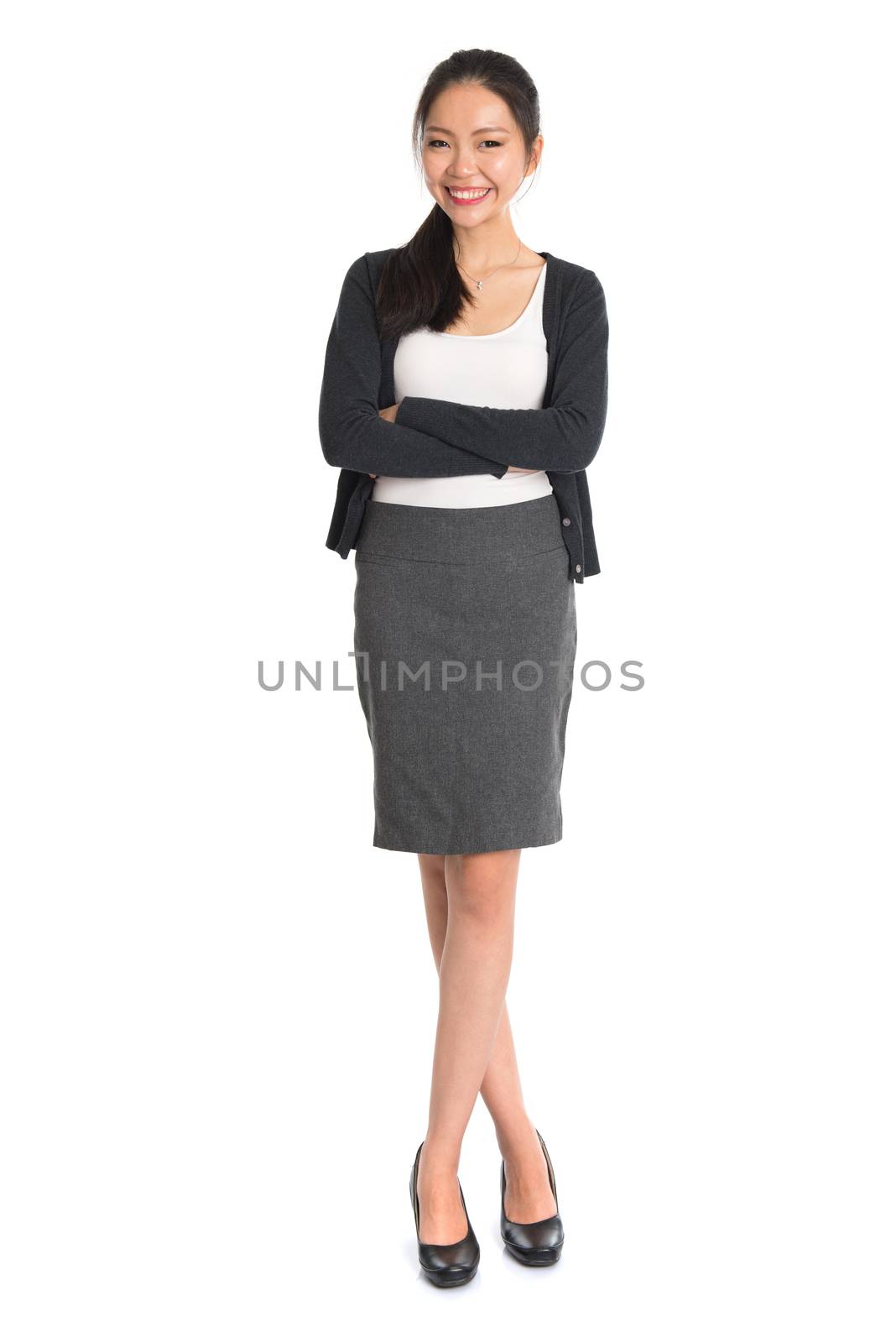 Full length portrait of young Asian girl arms crossed and smiling, standing isolated on white background.