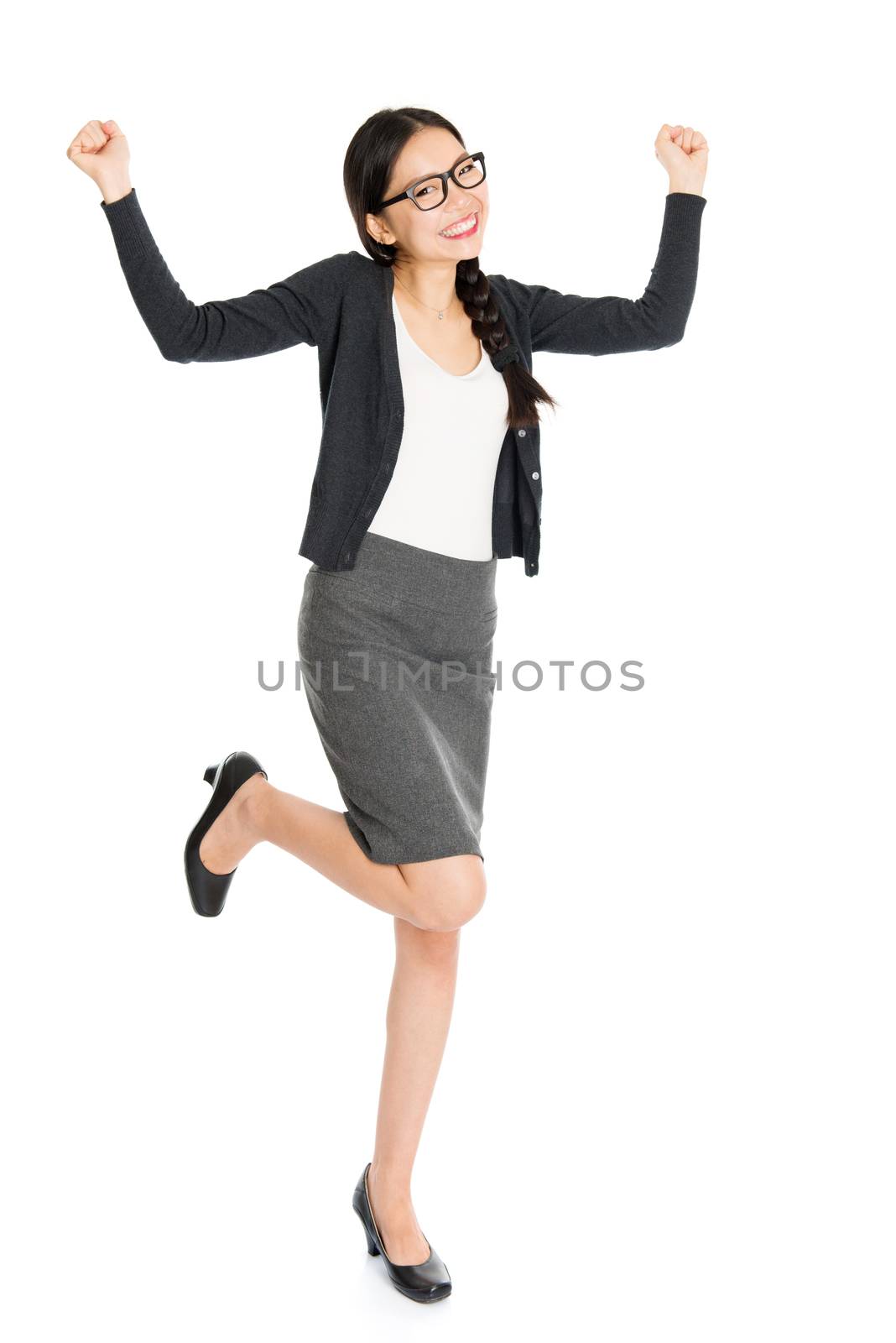 Full length portrait of young Asian female arms raised and jumping around, isolated on white background.