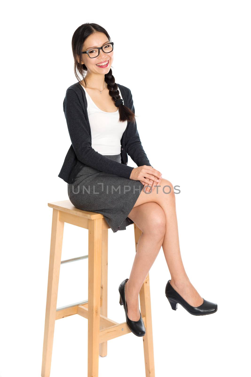 Full body portrait of young Asian woman leg crossed sitting on high chair, isolated on white background.