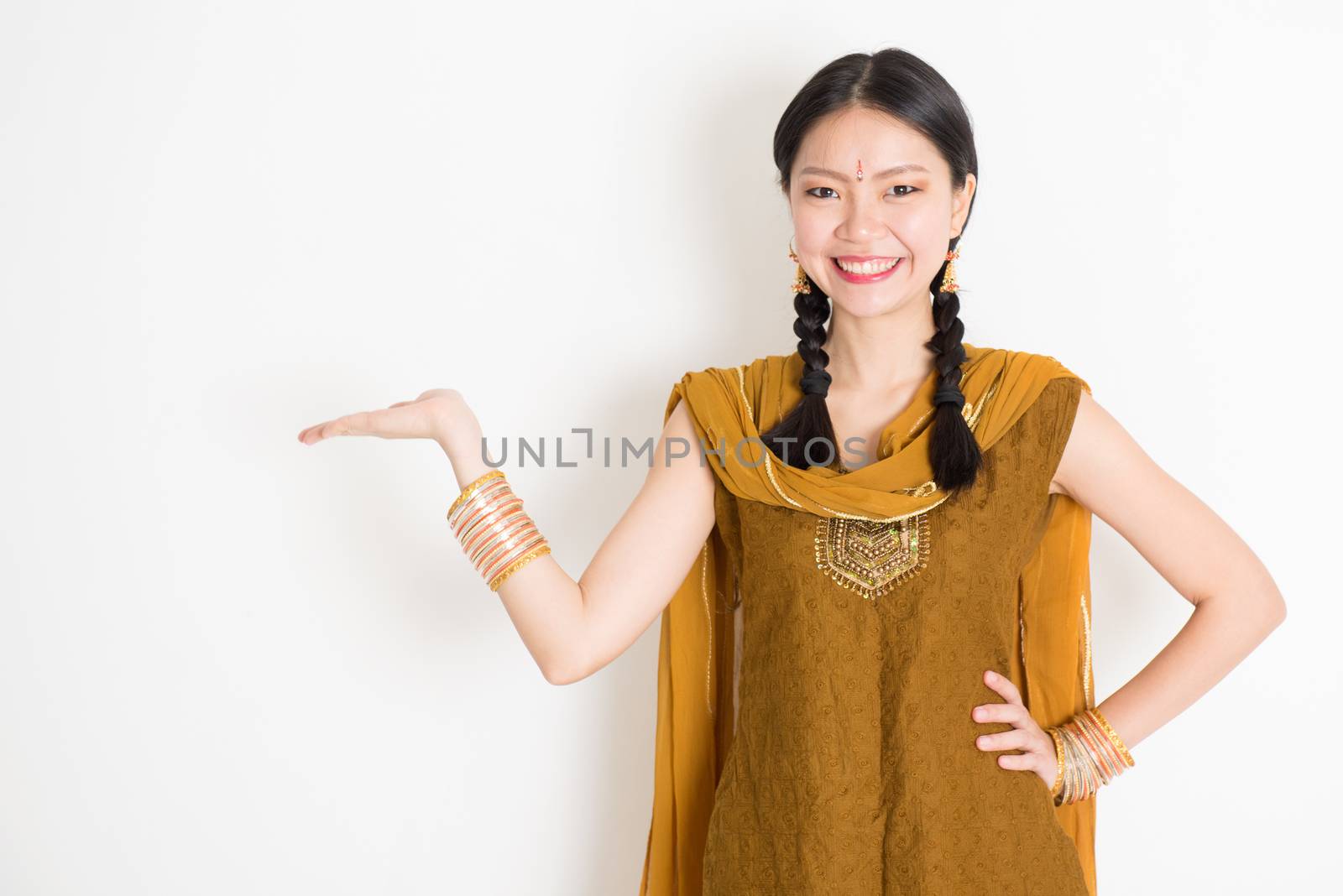 Portrait of young mixed race Indian Chinese female in traditional punjabi dress hand holding somethings, standing on plain white background.