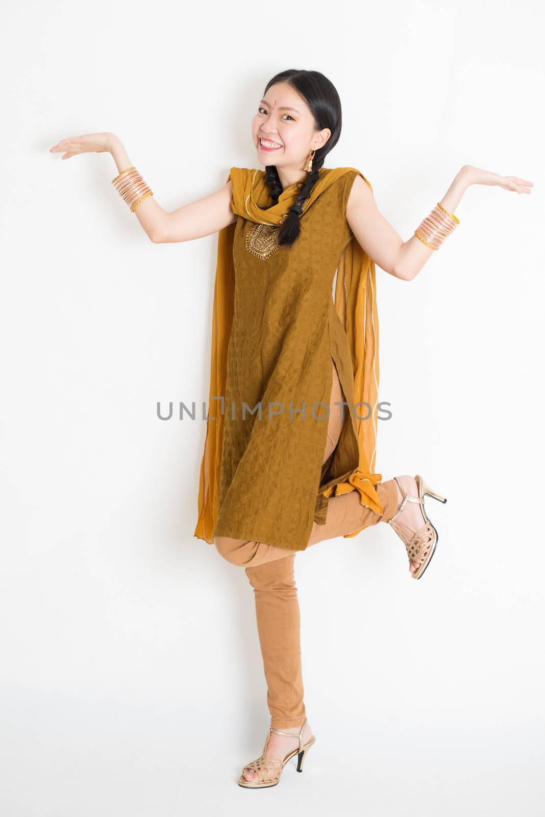 Portrait of excited mixed race Indian Chinese girl in traditional punjabi dress palms showing something, full length standing on plain white background.