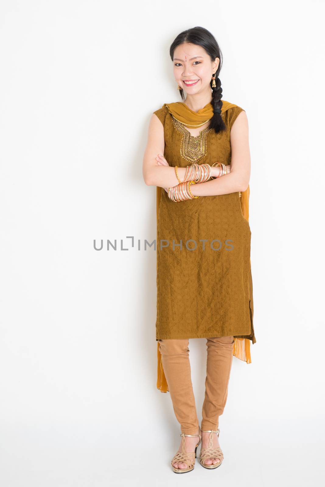 Portrait of young mixed race Indian Chinese female in traditional punjabi dress smiling, full length standing on plain white background.