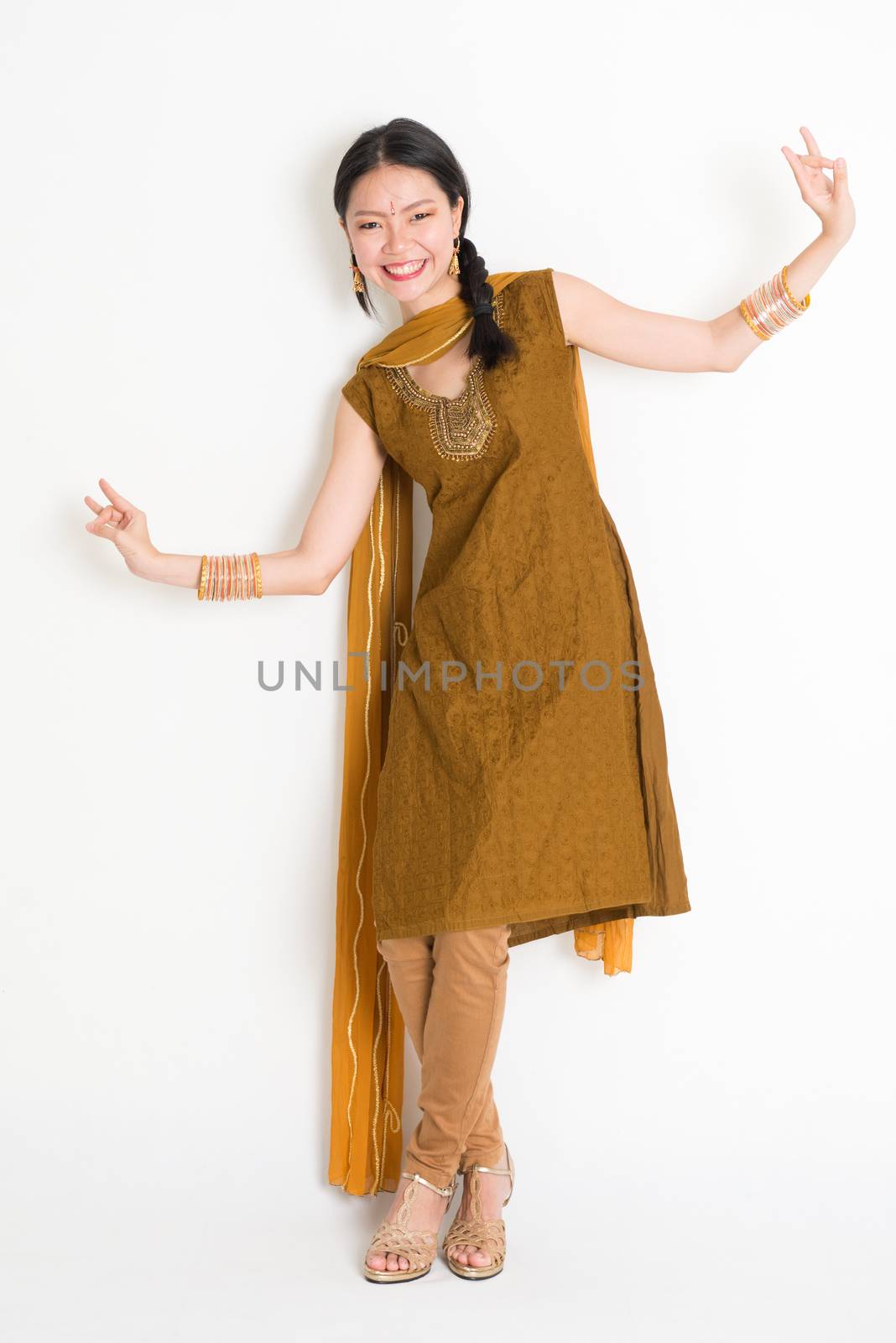Portrait of mixed race Indian Chinese woman in traditional punjabi dress dancing, full length standing on plain white background.