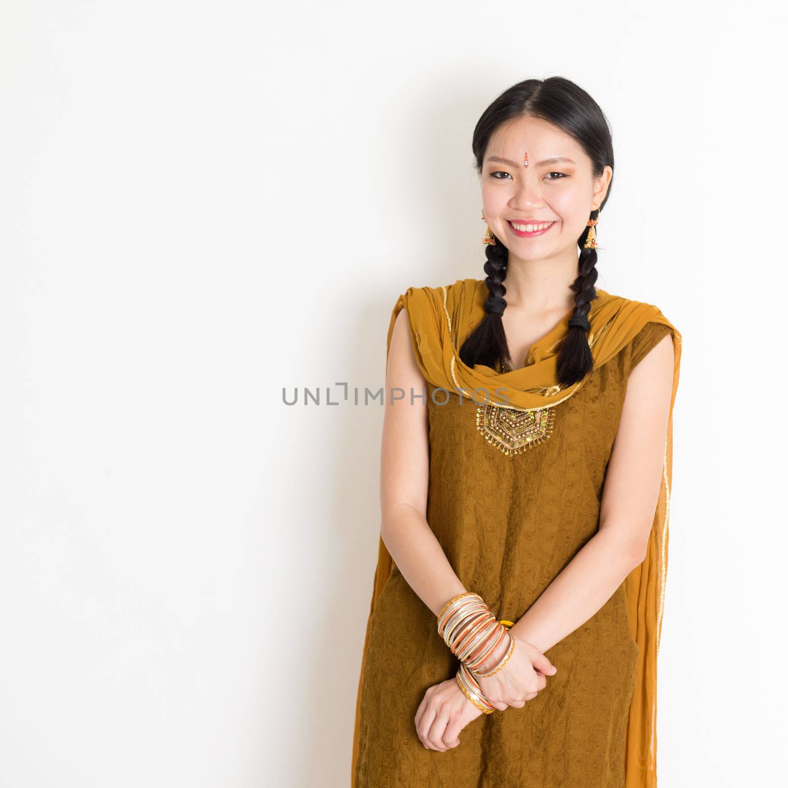Portrait of young mixed race Indian Chinese girl in traditional Punjabi dress smiling, standing on plain white background.